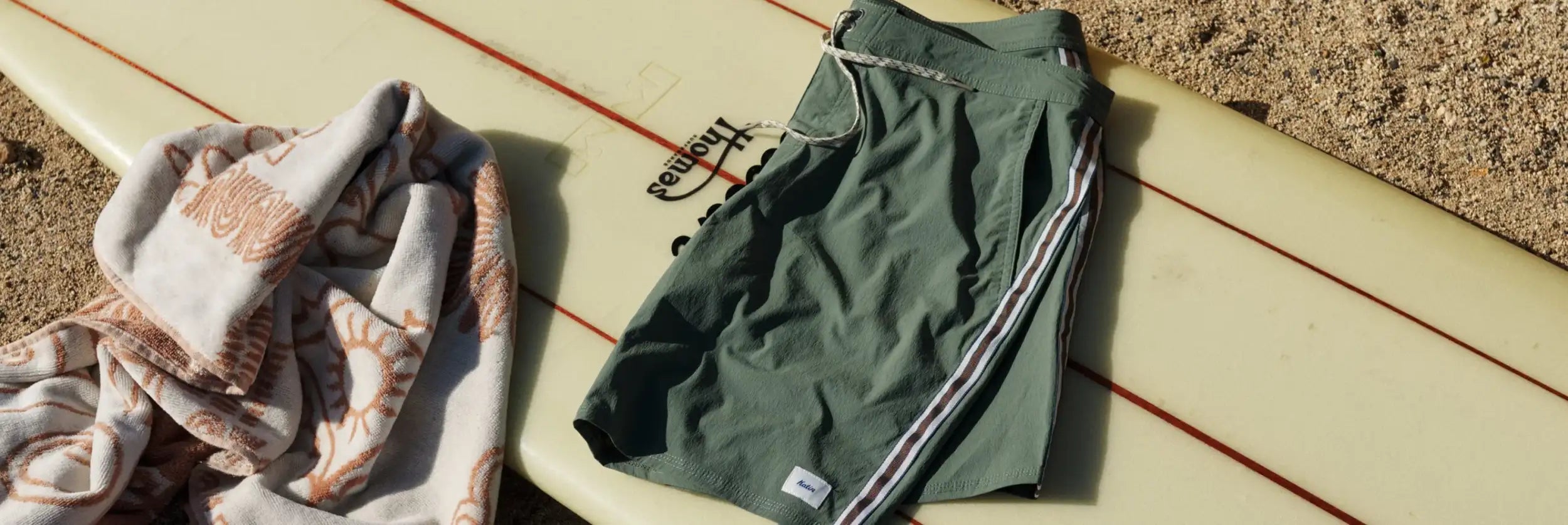 Maillots de bain vert olive avec des panneaux latéraux à rayures noires et blanches, avec une petite étiquette de marque sur la partie inférieure de la jambe droite.